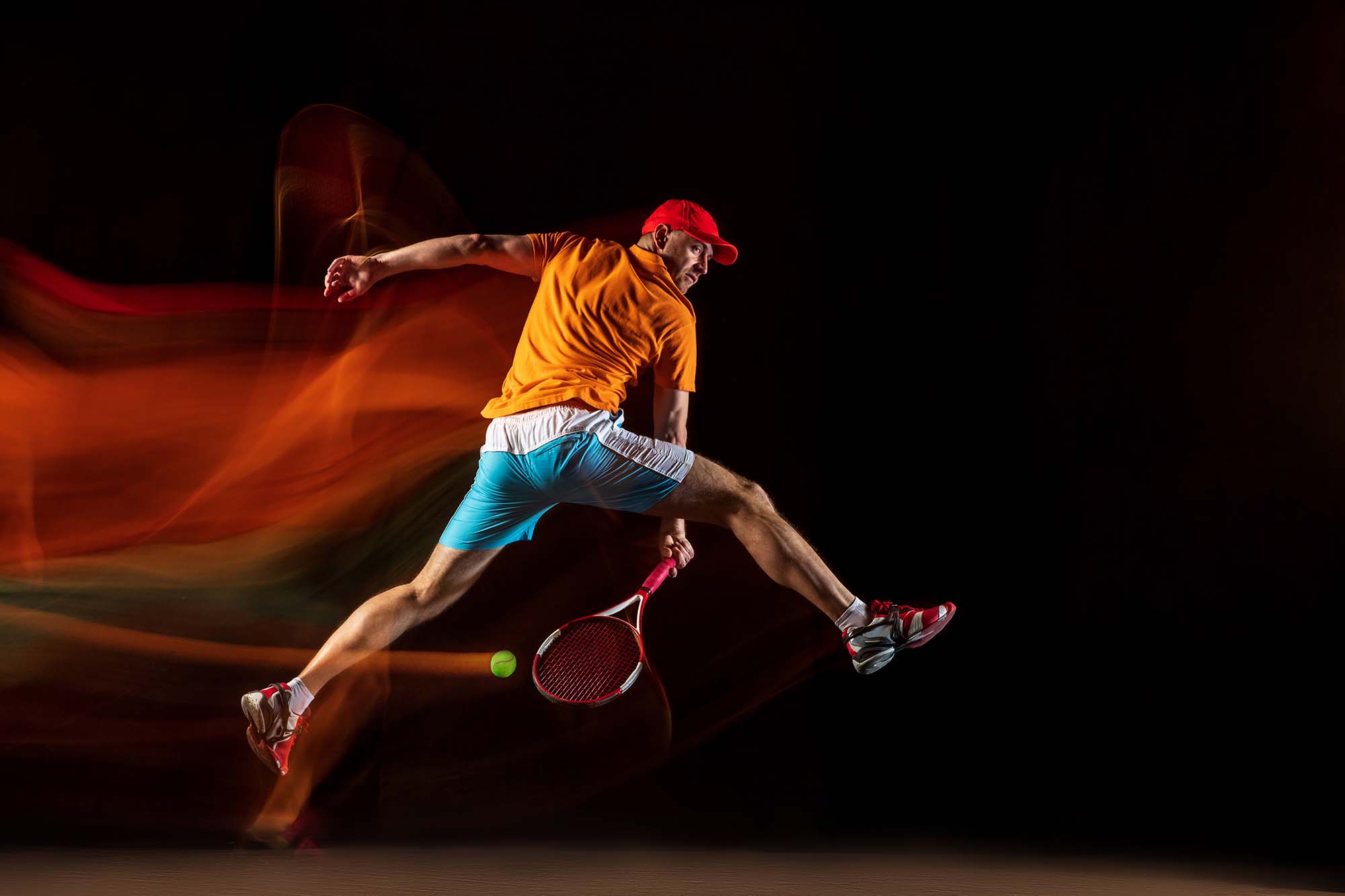 One caucasian man playing tennis isolated on black background in mixed light. Studio shot of fit young male player in motion or action during sport game. Concept of movement, sport, healthy lifestyle.